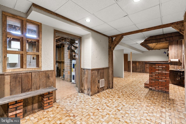 interior space with a drop ceiling, wood walls, and water heater