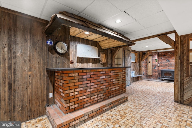 bar featuring a wood stove, a drop ceiling, and wood walls