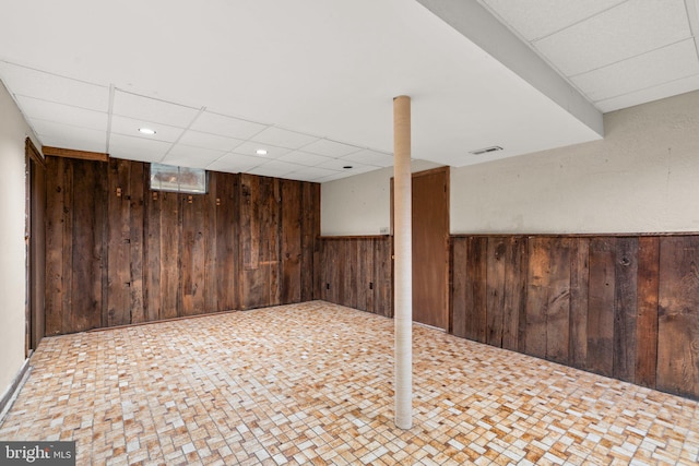 basement featuring wood walls and a drop ceiling