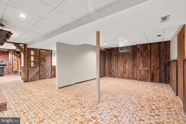 basement featuring a paneled ceiling and wooden walls