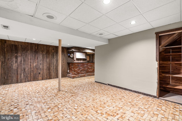 basement with wood walls and a drop ceiling