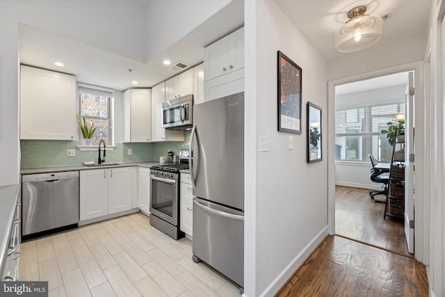 kitchen with backsplash, stainless steel appliances, white cabinetry, and sink