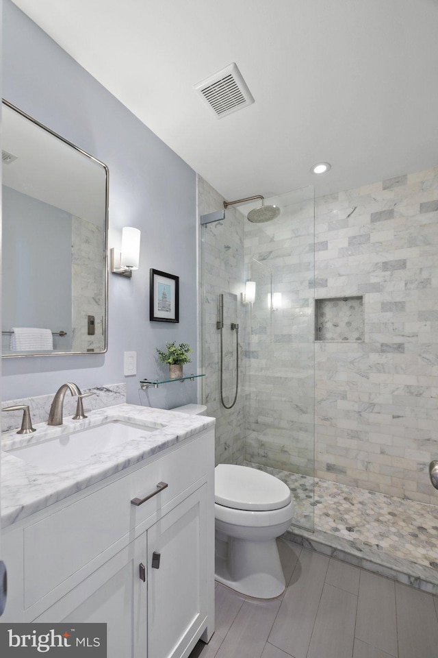 bathroom featuring a tile shower, vanity, and toilet