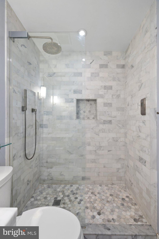 bathroom with a tile shower and toilet