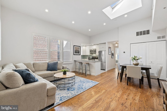 living room with light wood-type flooring, high vaulted ceiling, and a skylight