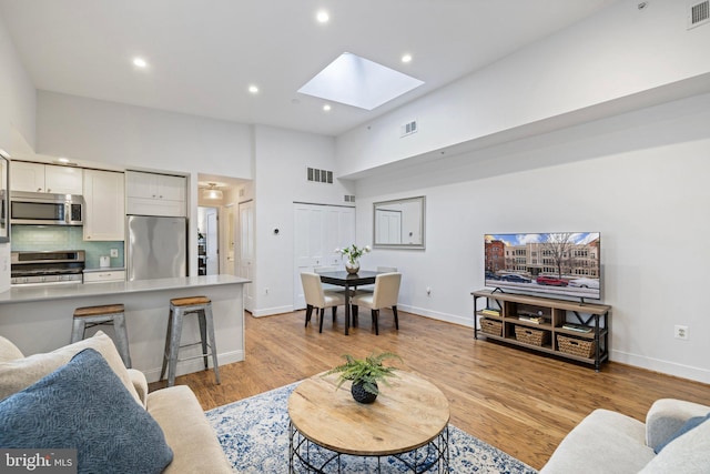 living room featuring a skylight, a towering ceiling, and light hardwood / wood-style floors