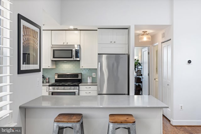 kitchen featuring white cabinets, appliances with stainless steel finishes, tasteful backsplash, and a kitchen breakfast bar