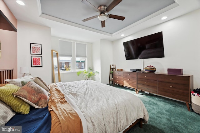 bedroom with ceiling fan, dark carpet, and a tray ceiling