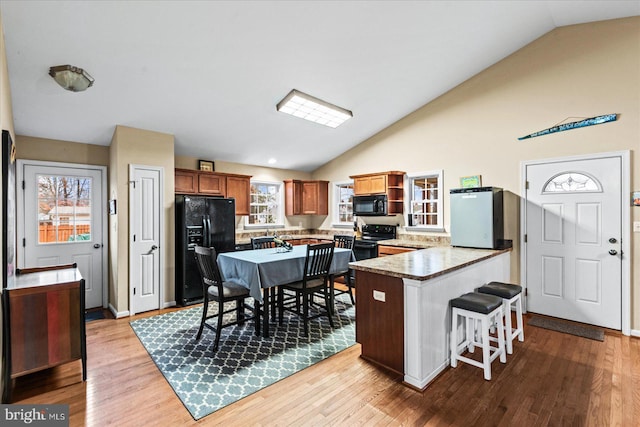 kitchen featuring black appliances, light hardwood / wood-style floors, kitchen peninsula, and vaulted ceiling