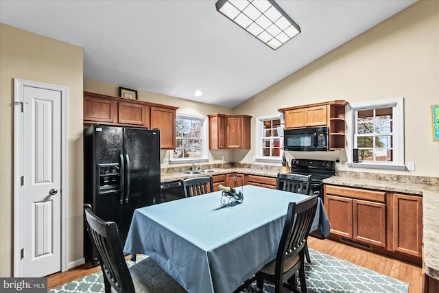 kitchen with black appliances, light wood-type flooring, lofted ceiling, and a wealth of natural light