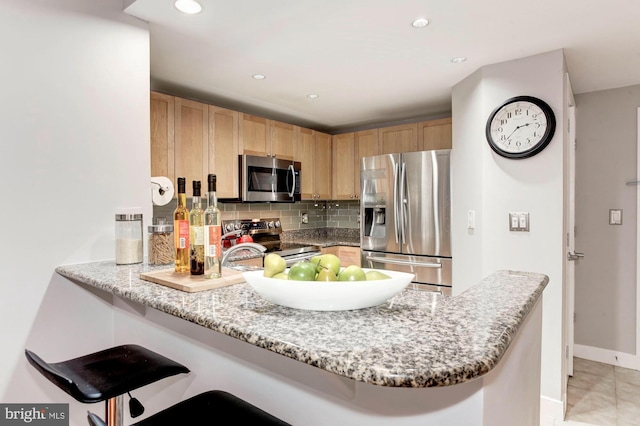 kitchen featuring kitchen peninsula, appliances with stainless steel finishes, backsplash, a kitchen bar, and light stone counters