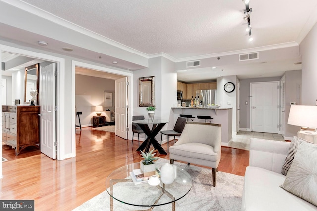 living room with a textured ceiling, light wood-type flooring, and ornamental molding