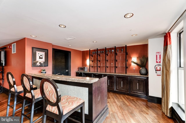 bar featuring plenty of natural light, light stone countertops, dark brown cabinetry, and light hardwood / wood-style flooring