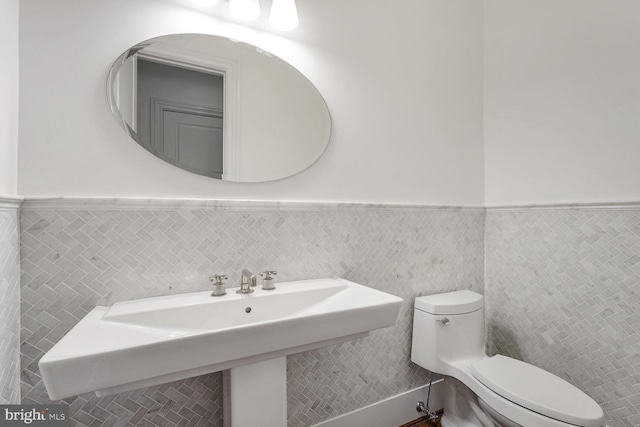 bathroom with toilet, sink, and tile walls