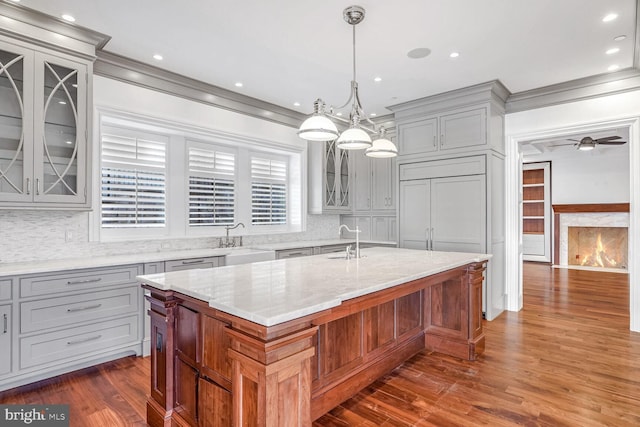 kitchen with pendant lighting, sink, light stone countertops, and a kitchen island with sink