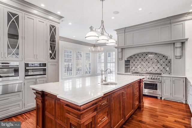 kitchen featuring sink, appliances with stainless steel finishes, backsplash, hanging light fixtures, and light stone countertops