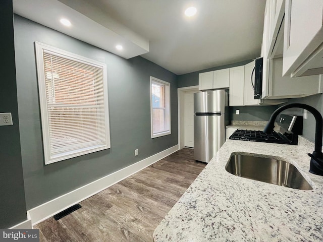 kitchen with wood-type flooring, light stone counters, white cabinetry, and stainless steel appliances