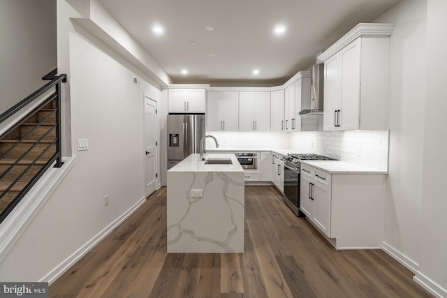 kitchen with white cabinetry, wall chimney exhaust hood, stainless steel appliances, dark hardwood / wood-style flooring, and a kitchen island with sink