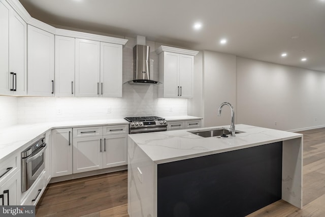 kitchen with wall chimney exhaust hood, a kitchen island with sink, sink, white cabinets, and hardwood / wood-style floors