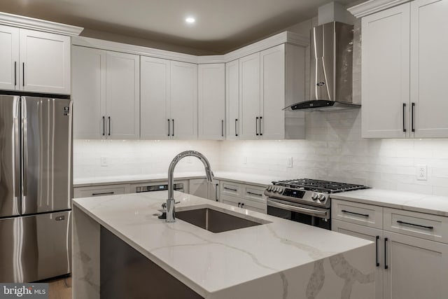 kitchen featuring light stone countertops, appliances with stainless steel finishes, wall chimney exhaust hood, sink, and white cabinets