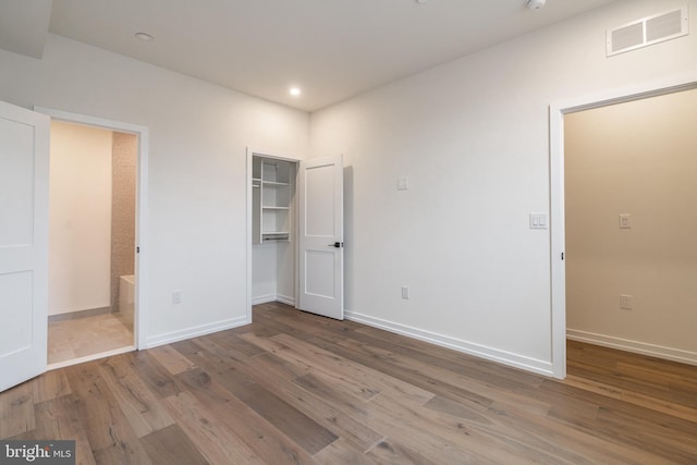 unfurnished bedroom with hardwood / wood-style floors, a spacious closet, and ensuite bath