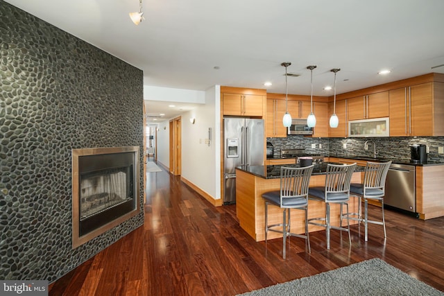 kitchen featuring a center island, dark wood-type flooring, pendant lighting, a tiled fireplace, and appliances with stainless steel finishes