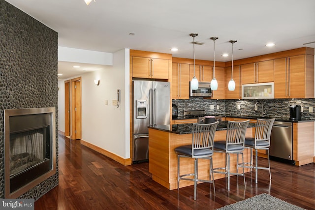 kitchen featuring pendant lighting, dark hardwood / wood-style floors, appliances with stainless steel finishes, a large fireplace, and a kitchen island