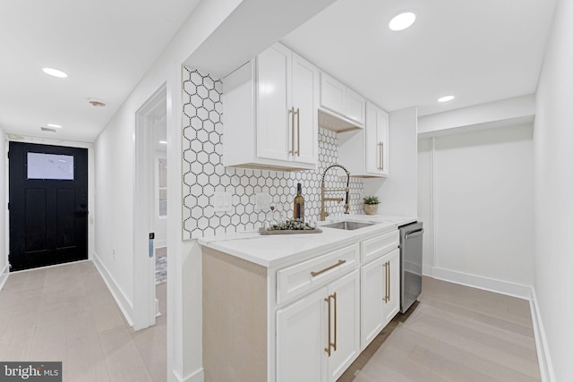 kitchen with white cabinetry, sink, tasteful backsplash, light hardwood / wood-style flooring, and stainless steel dishwasher