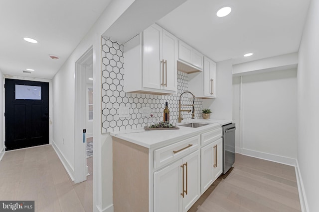 kitchen featuring tasteful backsplash, stainless steel dishwasher, sink, white cabinets, and light hardwood / wood-style floors