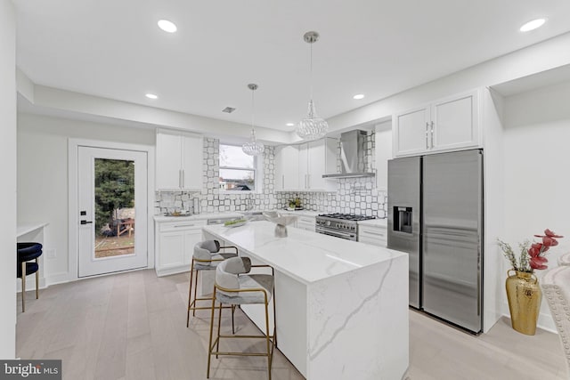 kitchen with wall chimney exhaust hood, a kitchen island, white cabinetry, and appliances with stainless steel finishes