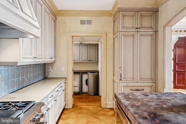 kitchen with washing machine and clothes dryer, tasteful backsplash, cream cabinets, light parquet flooring, and ornamental molding