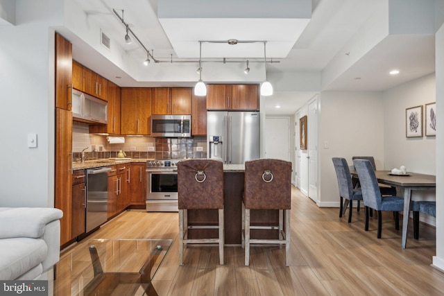 kitchen with hanging light fixtures, tasteful backsplash, a kitchen breakfast bar, light hardwood / wood-style flooring, and appliances with stainless steel finishes