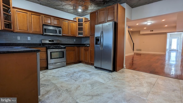 kitchen with light wood-type flooring, backsplash, stainless steel appliances, and dark stone counters