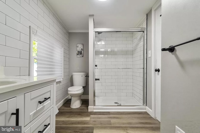 bathroom featuring toilet, hardwood / wood-style flooring, a shower with door, vanity, and ornamental molding