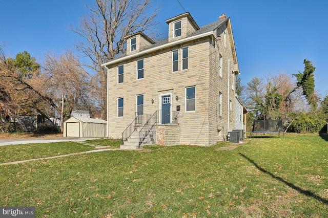 view of front facade featuring a trampoline, a front lawn, central AC unit, a garage, and an outbuilding