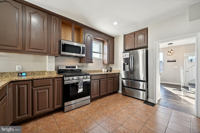 kitchen featuring pendant lighting, dark brown cabinetry, light stone countertops, and appliances with stainless steel finishes