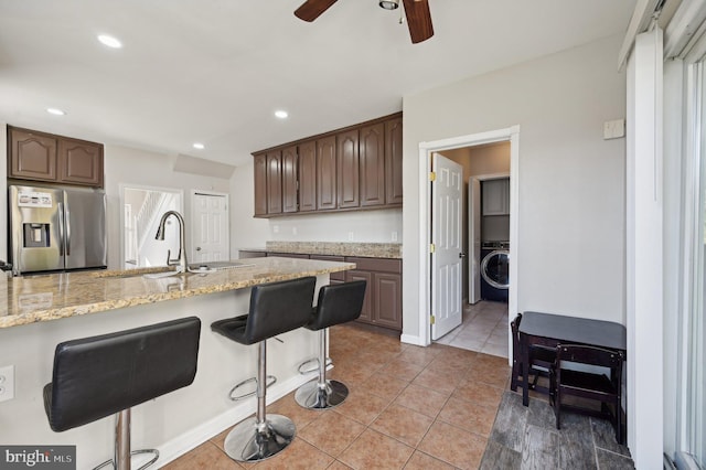 kitchen featuring stainless steel fridge, light stone counters, dark brown cabinets, sink, and washer / clothes dryer