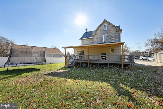 back of property featuring a lawn, a trampoline, and a wooden deck