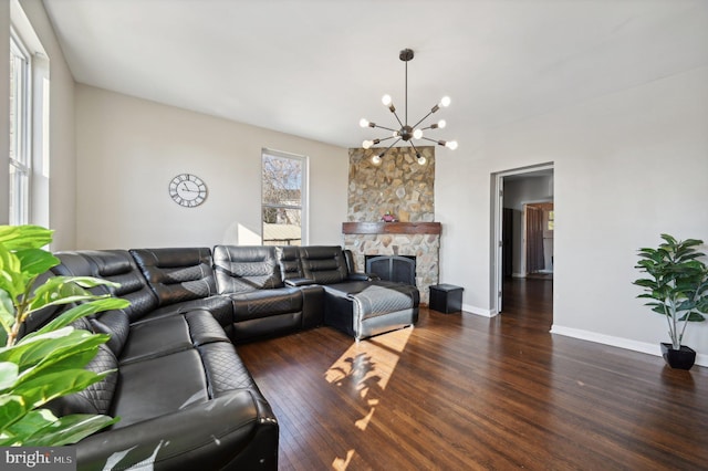 living room with a notable chandelier, a stone fireplace, and dark wood-type flooring