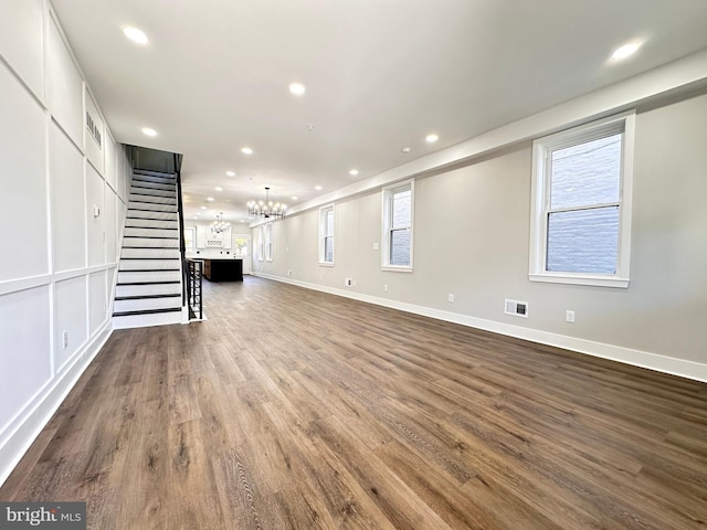 unfurnished living room featuring a notable chandelier and dark hardwood / wood-style flooring