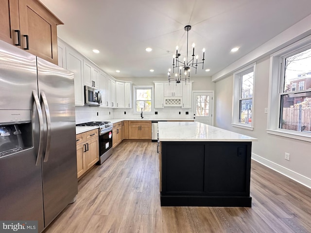 kitchen with light stone countertops, a center island, stainless steel appliances, pendant lighting, and light wood-type flooring