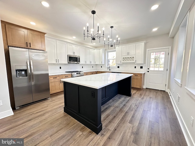 kitchen featuring a center island, white cabinets, hanging light fixtures, appliances with stainless steel finishes, and light stone counters