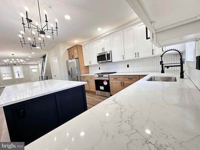 kitchen with sink, light stone counters, decorative light fixtures, white cabinets, and appliances with stainless steel finishes