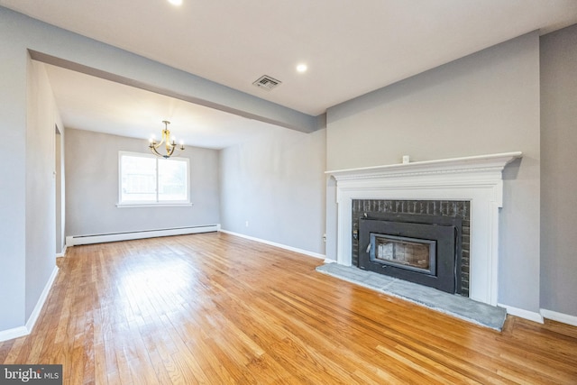 unfurnished living room featuring a chandelier, light hardwood / wood-style floors, a brick fireplace, and a baseboard heating unit