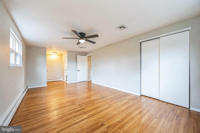 unfurnished bedroom with ceiling fan, a closet, light hardwood / wood-style floors, and a baseboard heating unit