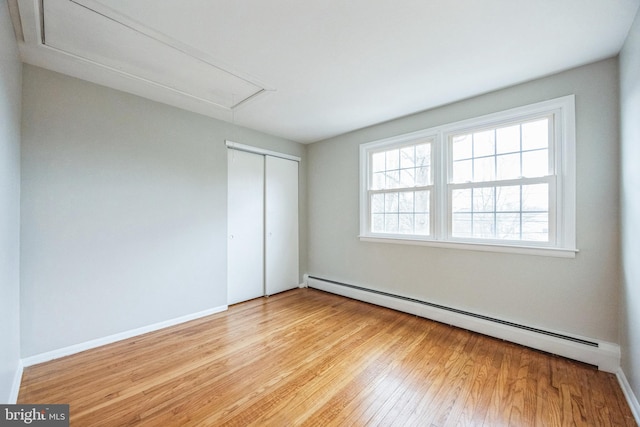 unfurnished bedroom featuring a closet, baseboard heating, and light hardwood / wood-style flooring