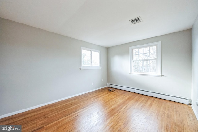 spare room featuring light hardwood / wood-style floors, baseboard heating, and a wealth of natural light