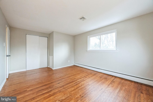 unfurnished bedroom with light hardwood / wood-style floors, baseboard heating, and a closet