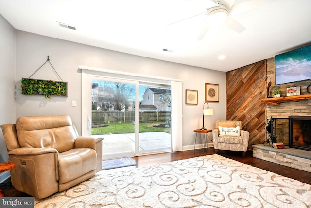 living room with a fireplace, hardwood / wood-style floors, ceiling fan, and wood walls