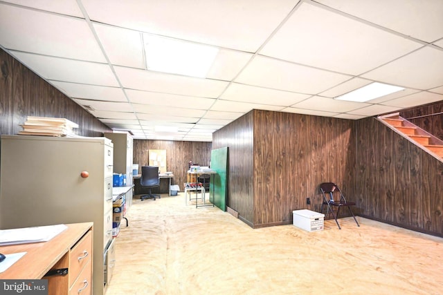 basement featuring a paneled ceiling, light colored carpet, and wooden walls